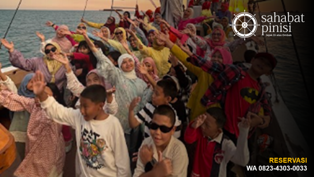 Rombongan wisatawan bergembira di dek kapal pinisi saat sunset sailing