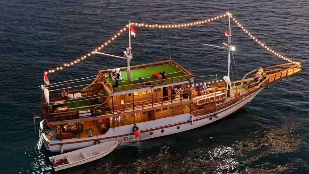 Kapal pinisi Sahabat Pinisi berlayar malam dengan lampu hias di laut Makassar
