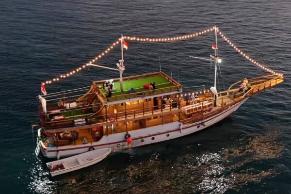 Kapal pinisi Sahabat Pinisi berlayar malam dengan lampu hias di laut Makassar