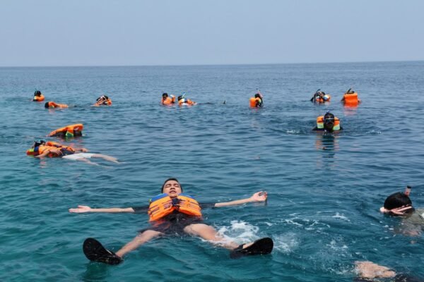 Tamu snorkeling memakai life jacket oranye di laut saat Full Day Sailing kapal pinisi Makassar