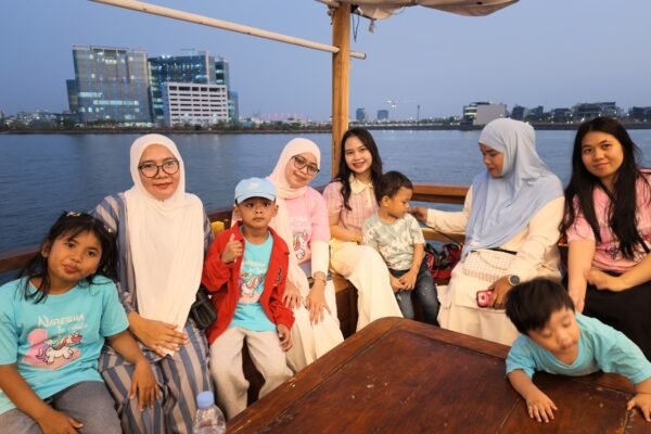 Keluarga duduk di kapal pinisi saat sunset dengan pemandangan gedung kota Makassar
